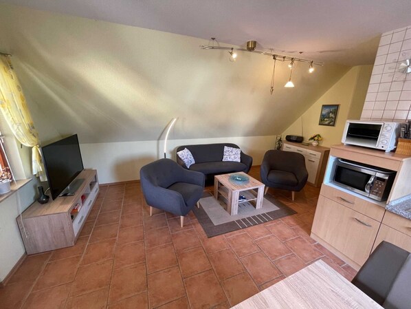 A compact living space with a sofa, two armchairs, a coffee table, a TV, and a kitchenette with a microwave and toaster.