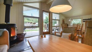 A cozy room with a wood-burning stove, large windows, a dining table, and chairs. - Lovely home in Ebeltoft with sauna (Ebeltoft)