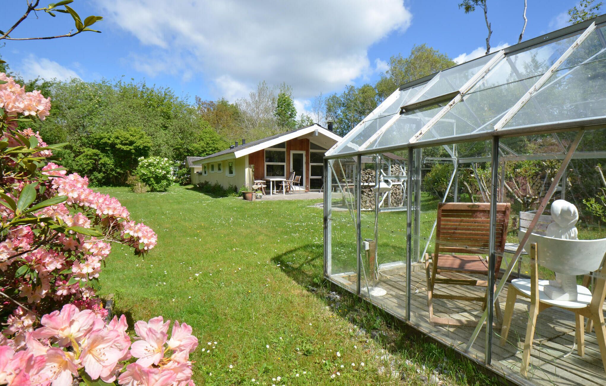 Une maison dotée d’une serre en verre, d’une pelouse et de fleurs roses.