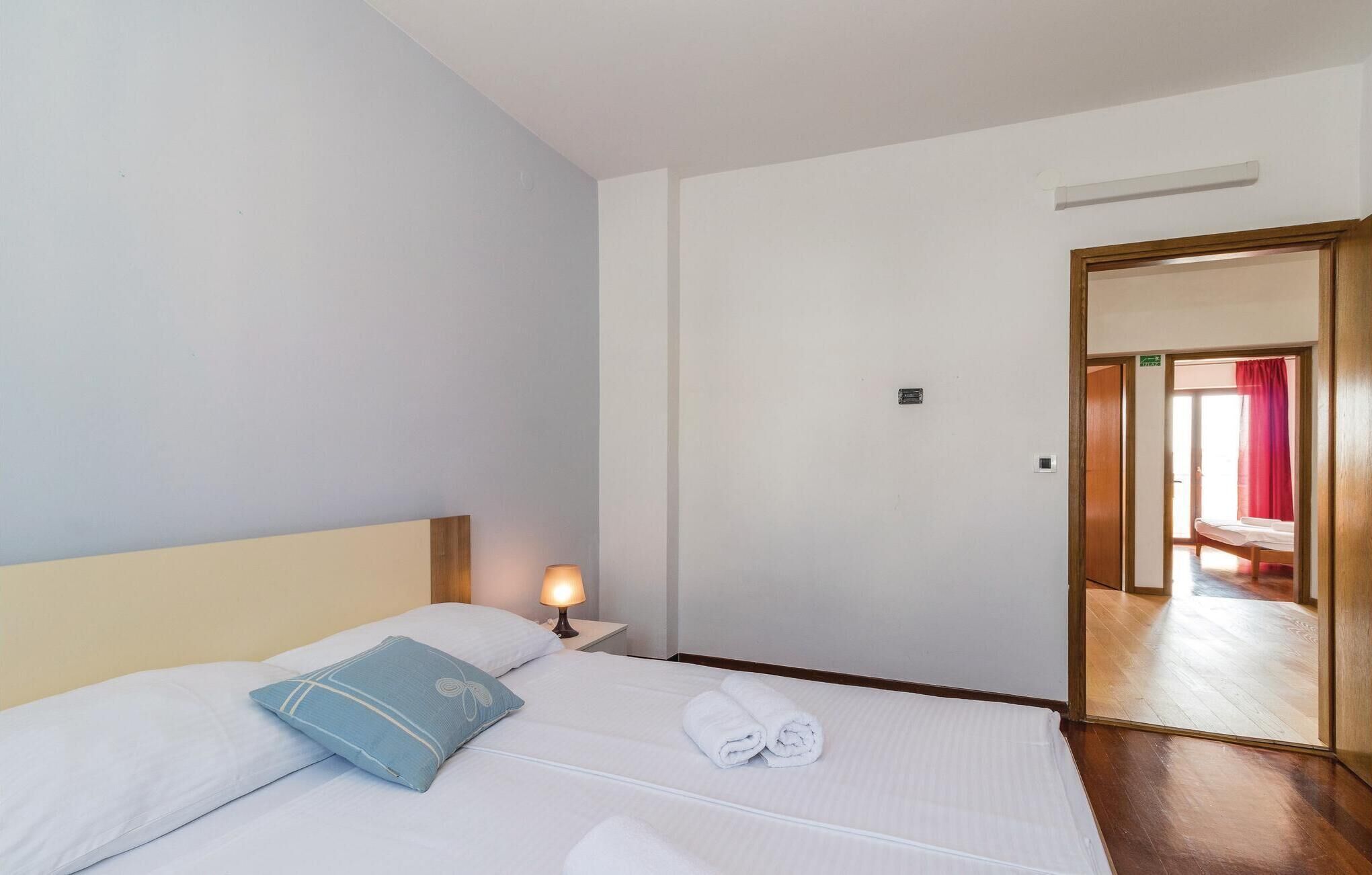 Une chambre d’hôtel avec un lit, une table de chevet avec une lampe, une porte en bois et une vue à travers la porte.
