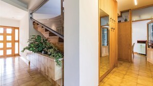 Een ruime hal met een houten trap, een ingebouwde plantenplank en een houten garderobe met glazen deuren.