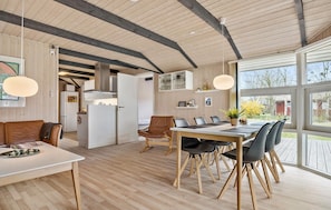 A modern kitchen with wooden beams, a dining area with a large table and chairs, and a view of the outdoors through large windows.