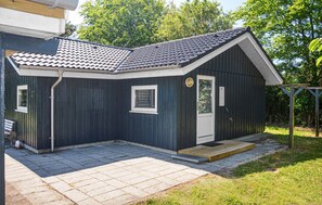 Un petit bâtiment de couleur sombre, avec un toit recouvert de tuiles, une porte d’entrée et une petite fenêtre.