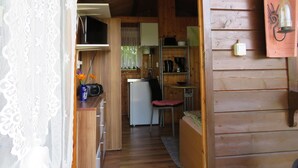 A cozy cabin interior with a wooden exterior, a kitchenette with a refrigerator, a microwave, and a coffee maker. There is a small dining area with a chair and a table.