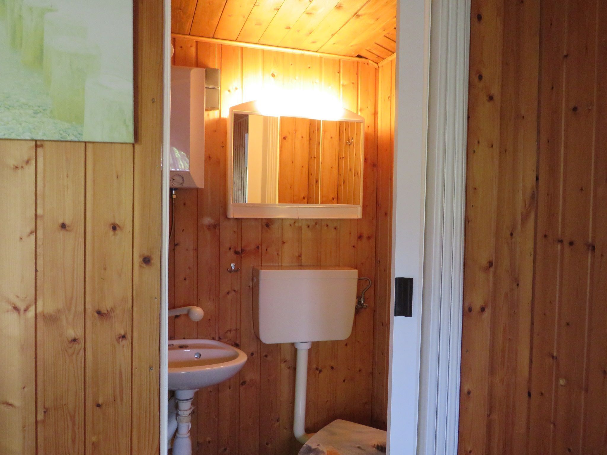 Une petite salle de bain aux murs lambrissés, avec un lavabo blanc, des toilettes et un miroir au-dessus du lavabo.