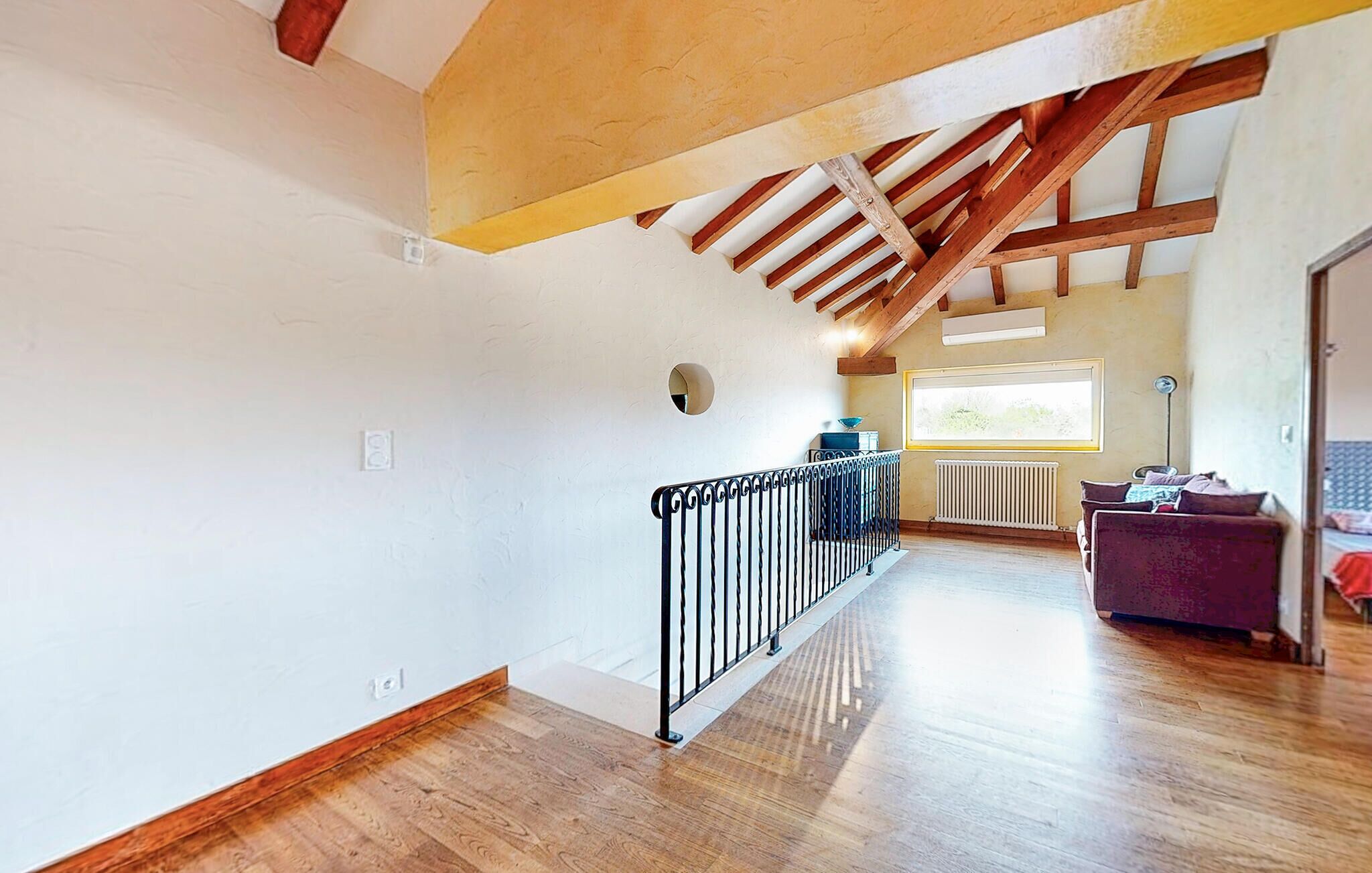 A spacious hallway with wooden floors, a metal railing, and a high ceiling with exposed beams.