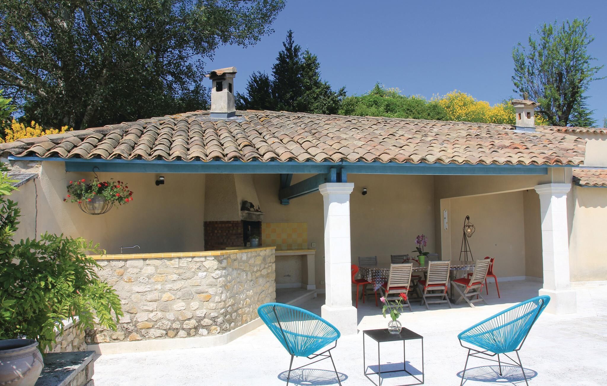 A covered outdoor patio with a tiled roof, stone walls, and two blue chairs.