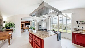 Une cuisine spacieuse dotée d’un grand îlot central, d’un four encastré et offrant une vue dégagée grâce à de grandes fenêtres.