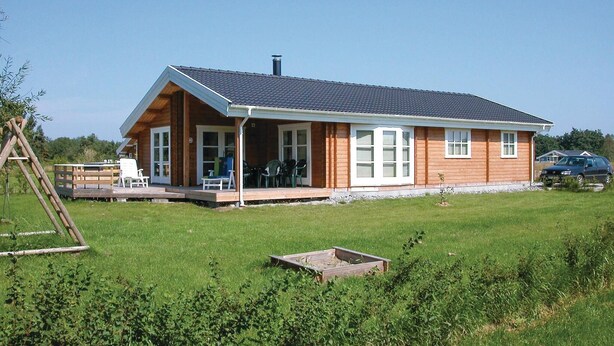 Ein Holzhaus mit Veranda, ein geparktes Auto in der Nähe und einem Rasen.