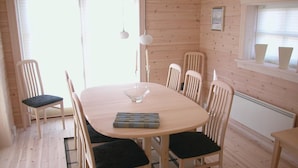 Ein Holzinterieur mit einem runden Tisch, sechs Stühlen, einer Glasvase und einem gerahmten Bild an der Wand.