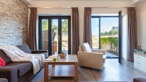 Ein modernes Wohnzimmer mit Sofa, Sessel und Couchtisch, einer Ziegelwand und großen Fenstern mit Vorhängen.