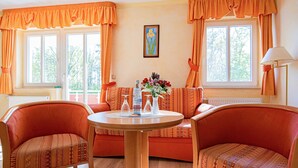 A room with two orange upholstered chairs, a round wooden table, and a sofa with patterned cushions. - 205 - Hotel Dünenschloss (Karlshagen)