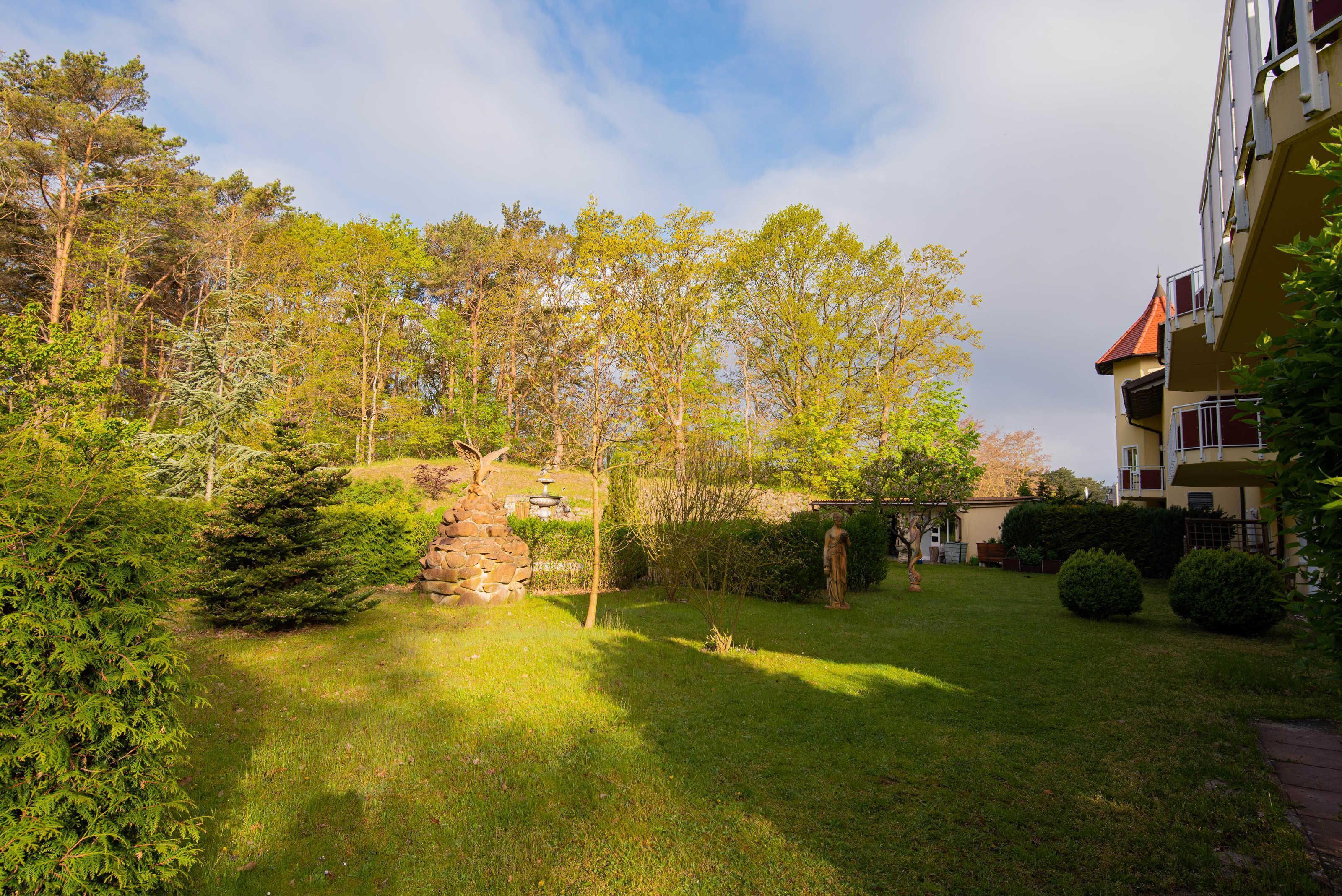 A well-maintained garden with a stone structure, surrounded by trees and a building with balconies.