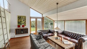A spacious living room with a high ceiling, leather sofas, a wooden coffee table, and a painting on the wall. - 3 bedroom nice home in Ebeltoft (Ebeltoft)