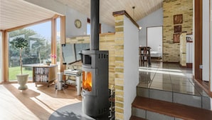 A cozy room with a wood-burning stove, a bookshelf, and a view of the outdoors. - 3 bedroom nice home in Ebeltoft (Ebeltoft)