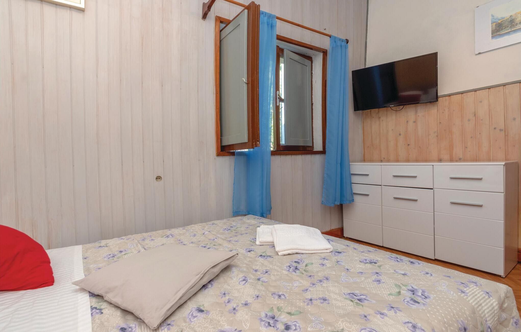 Ein Schlafzimmer mit einem Bett, einem Schminktisch, einem Fernseher und einem Fenster mit Vorhängen.