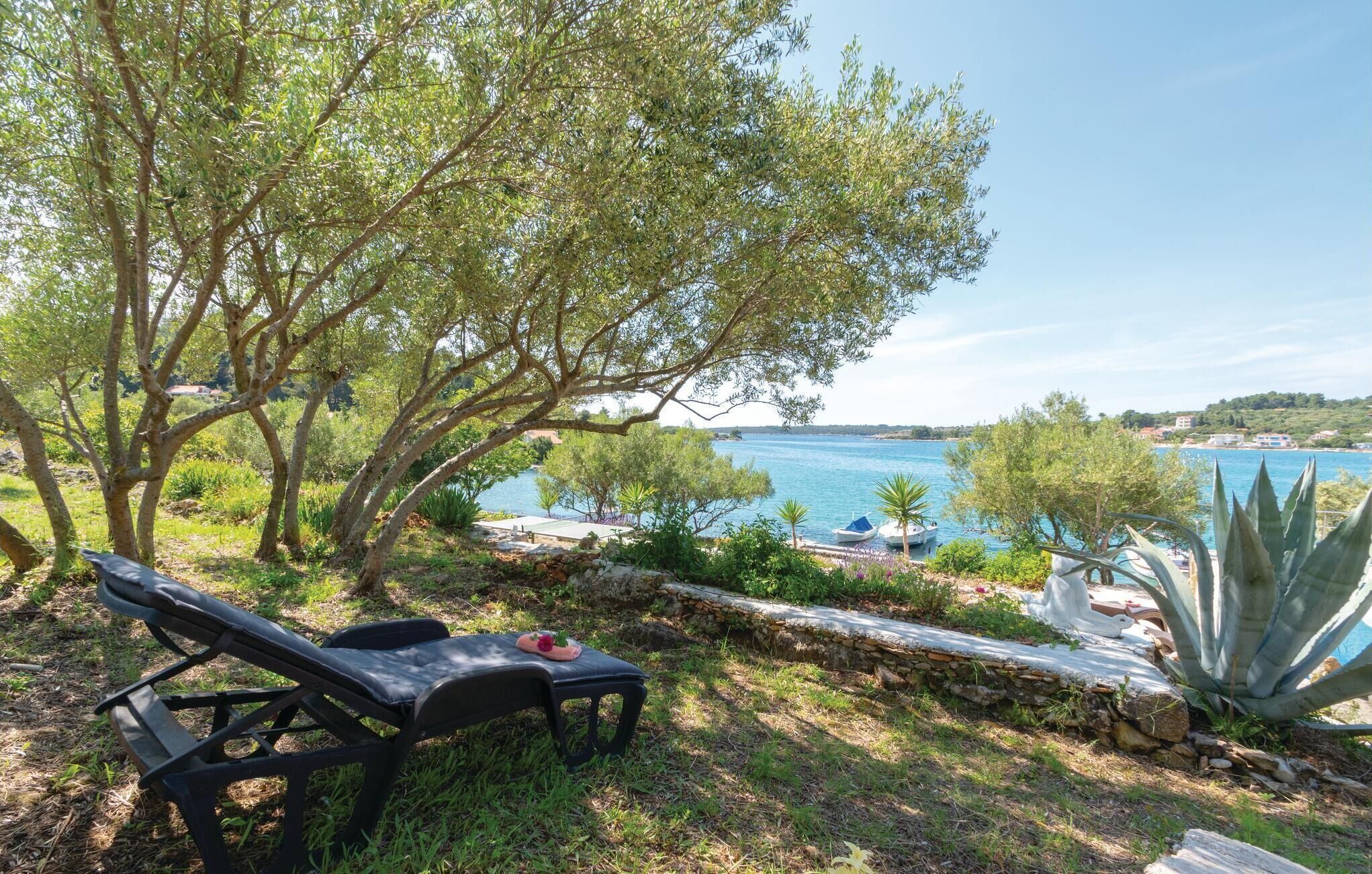 A bench overlooking a body of water with boats, surrounded by greenery and a clear sky.