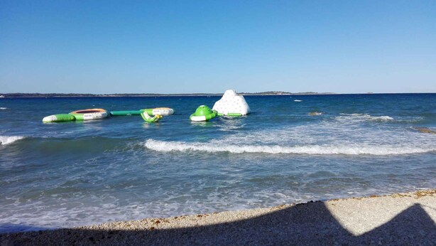 Ein Strand mit mehreren aufblasbaren Wasserspielen im Wasser.