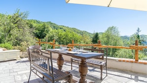 Un espace de restauration en plein air, avec une table et des chaises, entouré d’une clôture en bois et offrant une vue sur une colline boisée.