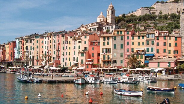Une promenade en bord de mer bordée de bâtiments aux couleurs vives, un quai où sont amarrés des bateaux et une tour imposante.