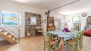 Un coin repas avec une table dressée pour quatre personnes, entouré de chaises vertes, d’un mur en pierre et offrant une vue sur l’extérieur.