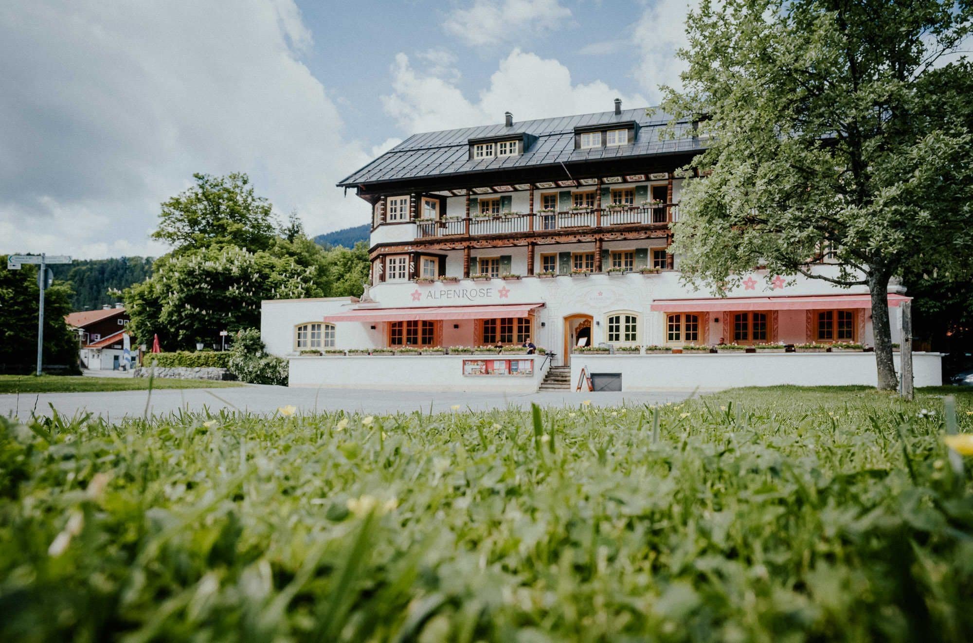 Un edificio tradicional con un balcón, un cartel que dice 'ALPENROSE' y una zona de entrada empavedada.