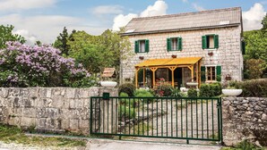 Une maison en pierre avec un toit de tuiles, des volets verts et un porche en bois.