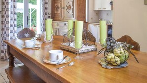 Une table à manger en bois, agrémentée d’un panier à fruits en fil de fer, d’un plateau décoratif et de bougies vertes.