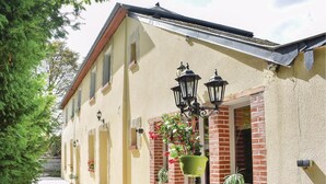 Un bâtiment à la façade beige, agrémentée de détails en briques rouges et doté de nombreuses fenêtres. On peut apercevoir des luminaires extérieurs et des plantes en pot.