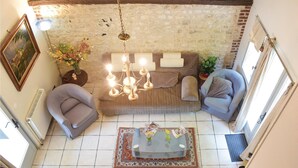 Un salon chaleureux avec un mur en pierre, un canapé, deux fauteuils, une table basse en verre et un luminaire suspendu.