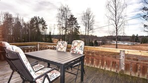 A wooden deck with a table and chairs, overlooking a forested area with a river in the background. - 3 bedroom beautiful home in årjäng (Årjäng)