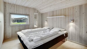Ein Schlafzimmer mit Holzboden, einem Bett mit weißer Bettwäsche, einem Fenster mit Blick auf ein Haus und einem Wandregal.