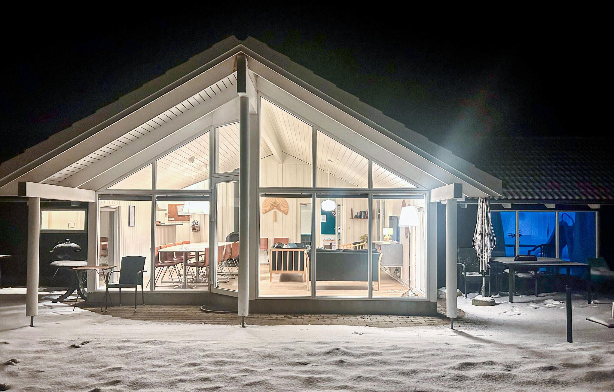 Una casa moderna con un gran ventanal, un comedor con sillas naranjas y una cocina a la vista.