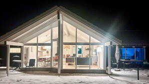 Ein modernes Haus mit großer Glasfront, einem Essbereich mit orangefarbenen Stühlen und einer sichtbaren Küche.