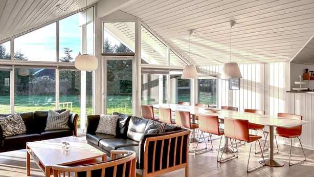 Ein großzügiger Wohnbereich im modernen Stil mit einer Ledersofa, Holzstühlen, einem Esstisch und großen Fenstern mit Blick ins Freie.