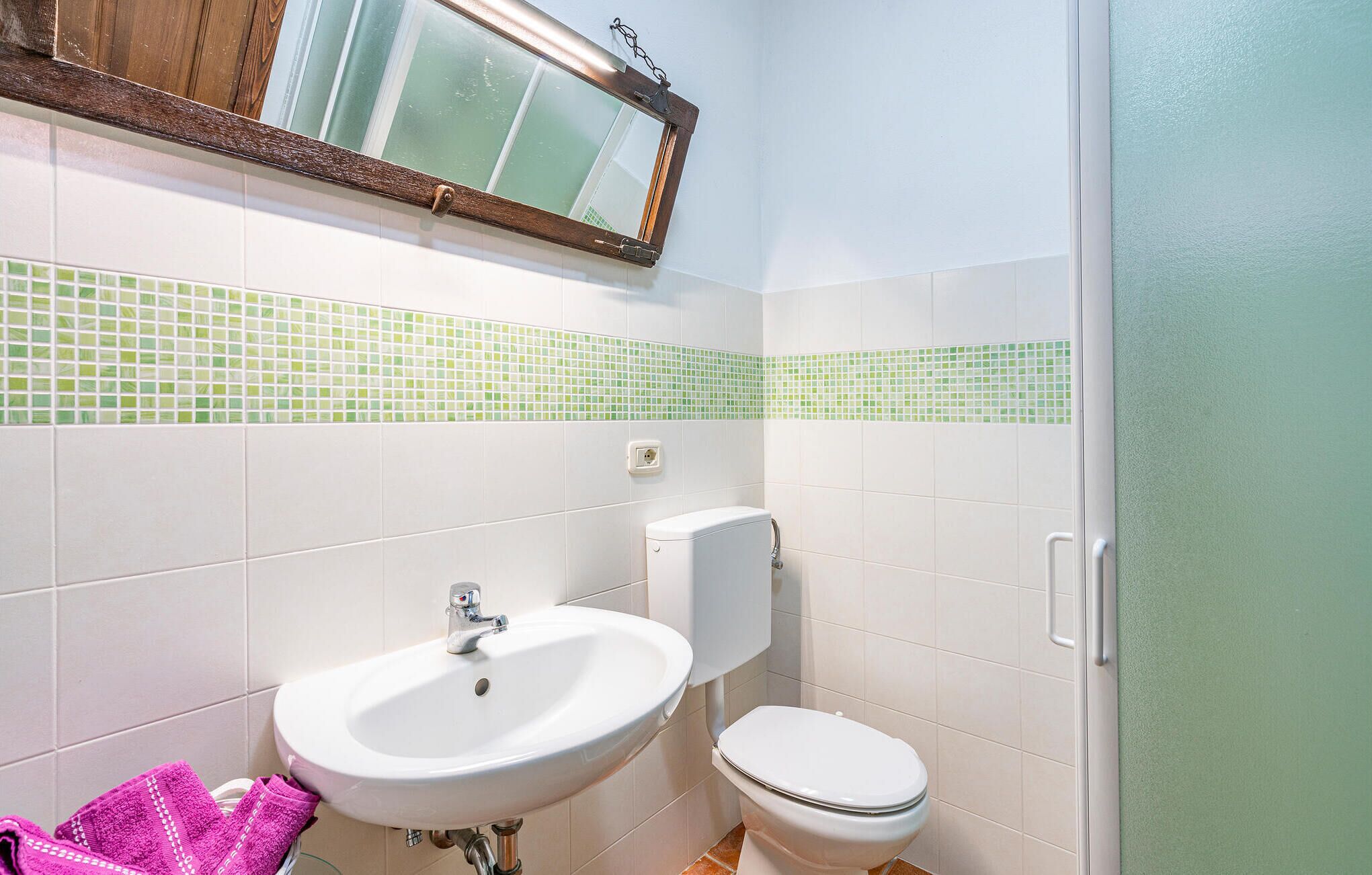 A bathroom with a white sink, toilet, and green-tiled backsplash.