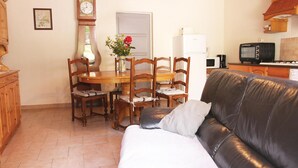 Un salon chaleureux avec un canapé en cuir, une table à manger en bois et des chaises. Une horloge et un vase avec des fleurs sont accrochés au mur.