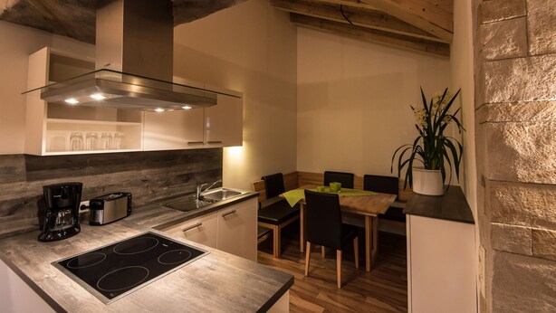 Una cocina moderna con estufa integrada, extractor de acero inoxidable y comedor con mesa y sillas de madera.
