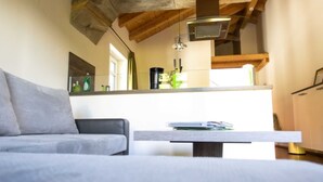 Una sala de estar moderna con un sofá gris, techo de madera y una cocina al fondo.