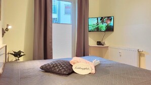A bedroom with a bed, a television on the wall, and a window with curtains. - (164) 2-room apartment - apartment complex Yachthafenresidenz (Kühlungsborn)