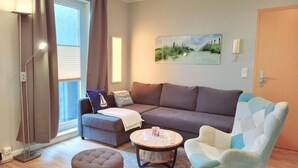 A living room with a sofa, armchair, ottoman, and a round coffee table. - (164) 2-room apartment - apartment complex Yachthafenresidenz (Kühlungsborn)