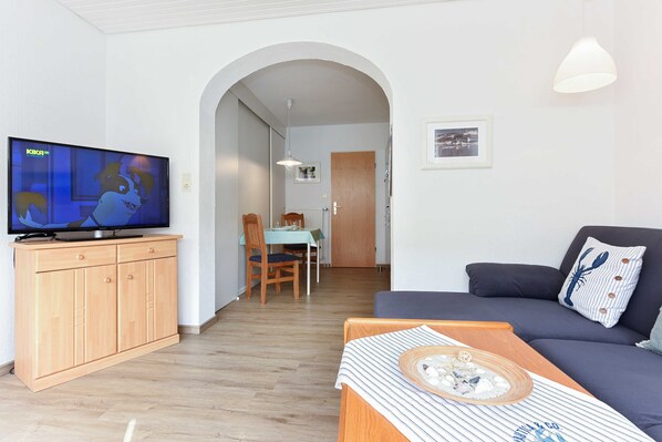 A living room with a television, a sofa, a dining table with chairs, and a wooden cabinet.