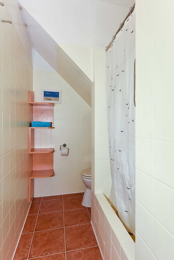 Un baño pequeño con un inodoro, una cortina de ducha y una repisa con toallas.