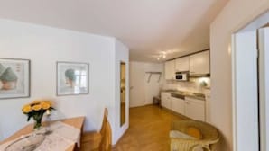 A modern kitchen with white cabinets and a microwave. There is a dining area with a table and chairs, and a vase with flowers.