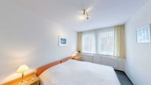 A hotel room with a bed, a nightstand, a lamp, and a window with curtains.