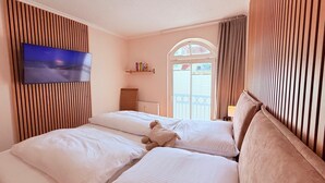 A hotel room with two beds, a TV mounted on the wall, a window with curtains, and a view of the outside. - (5) 3-room apartment south-facing balcony - apartment house Atlantic (Kühlungsborn)