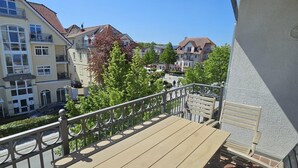 A balcony with a wooden table and chairs, a railing, and a view of surrounding buildings. - (5) 3-room apartment south-facing balcony - apartment house Atlantic (Kühlungsborn)