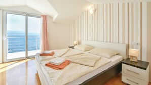A bedroom with a large bed, a nightstand, a lamp, and a view of the sea through a sliding door. - 2 bedroom awesome apartment in Stanici (Stanici)