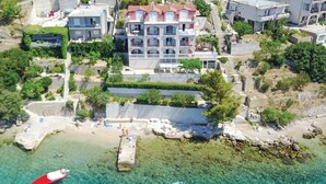 An aerial view of a coastal area with a large building with multiple balconies, clear turquoise waters, and boats anchored nearby. - 2 bedroom awesome apartment in Stanici (Stanici)