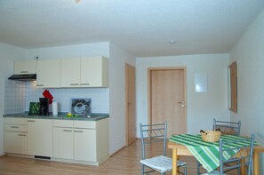 A compact kitchen with white cabinets, a wooden door, and a dining area with a table and chairs.